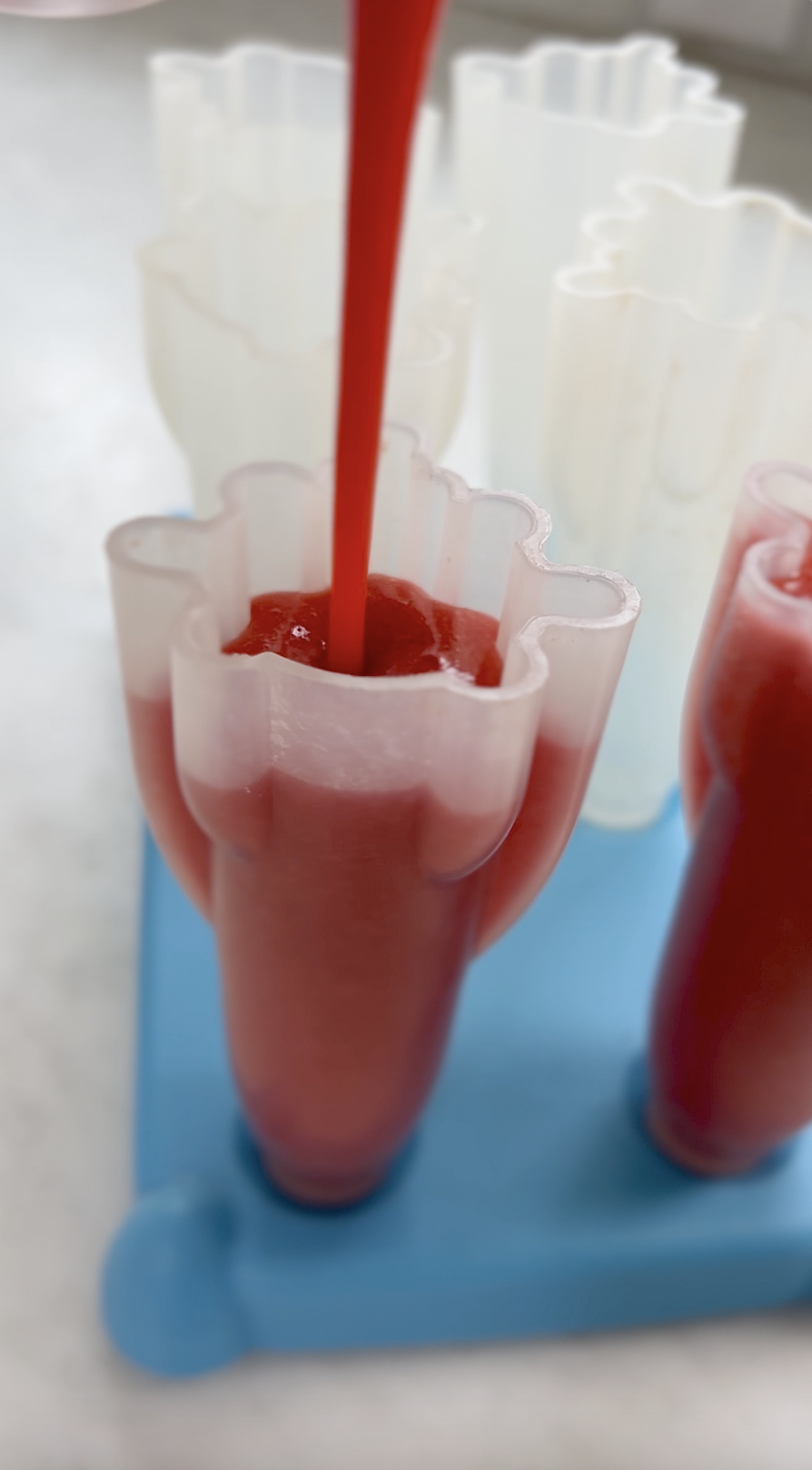 Pouring strawberry puree into popsicle mold.