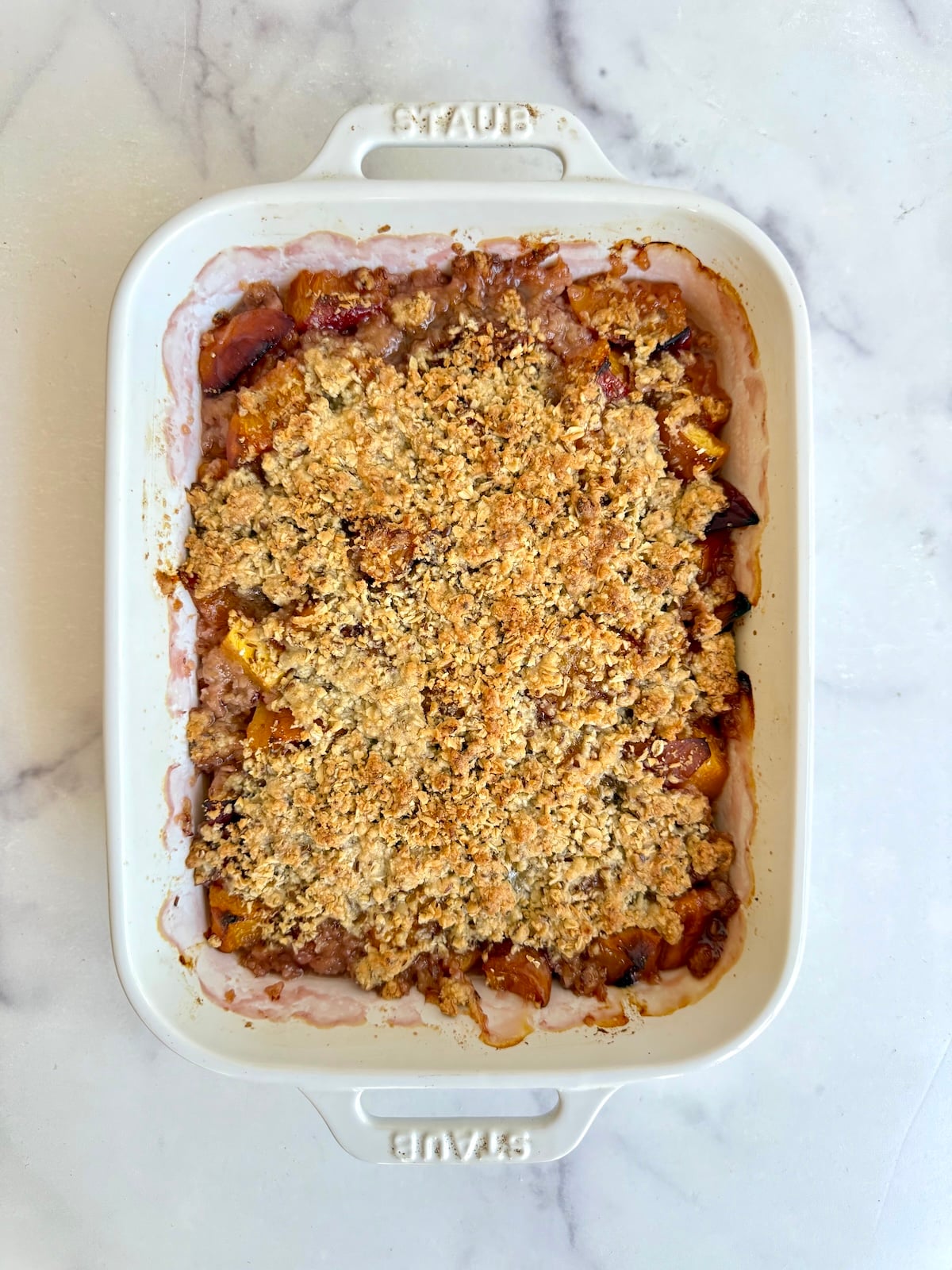 Golden baked peach crumble with a crisp oat topping in a white baking dish.