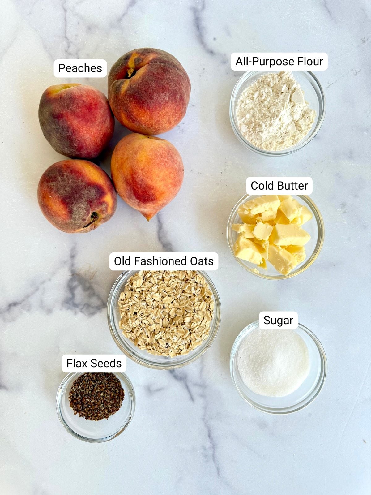 Ingredients for peach crumble: fresh peaches, all-purpose flour, cold butter, old fashioned oats, flax seeds, and sugar in glass bowls.