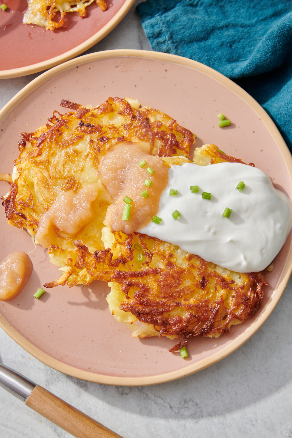 Latke on plate topped with applesauce, sour cream and chives.