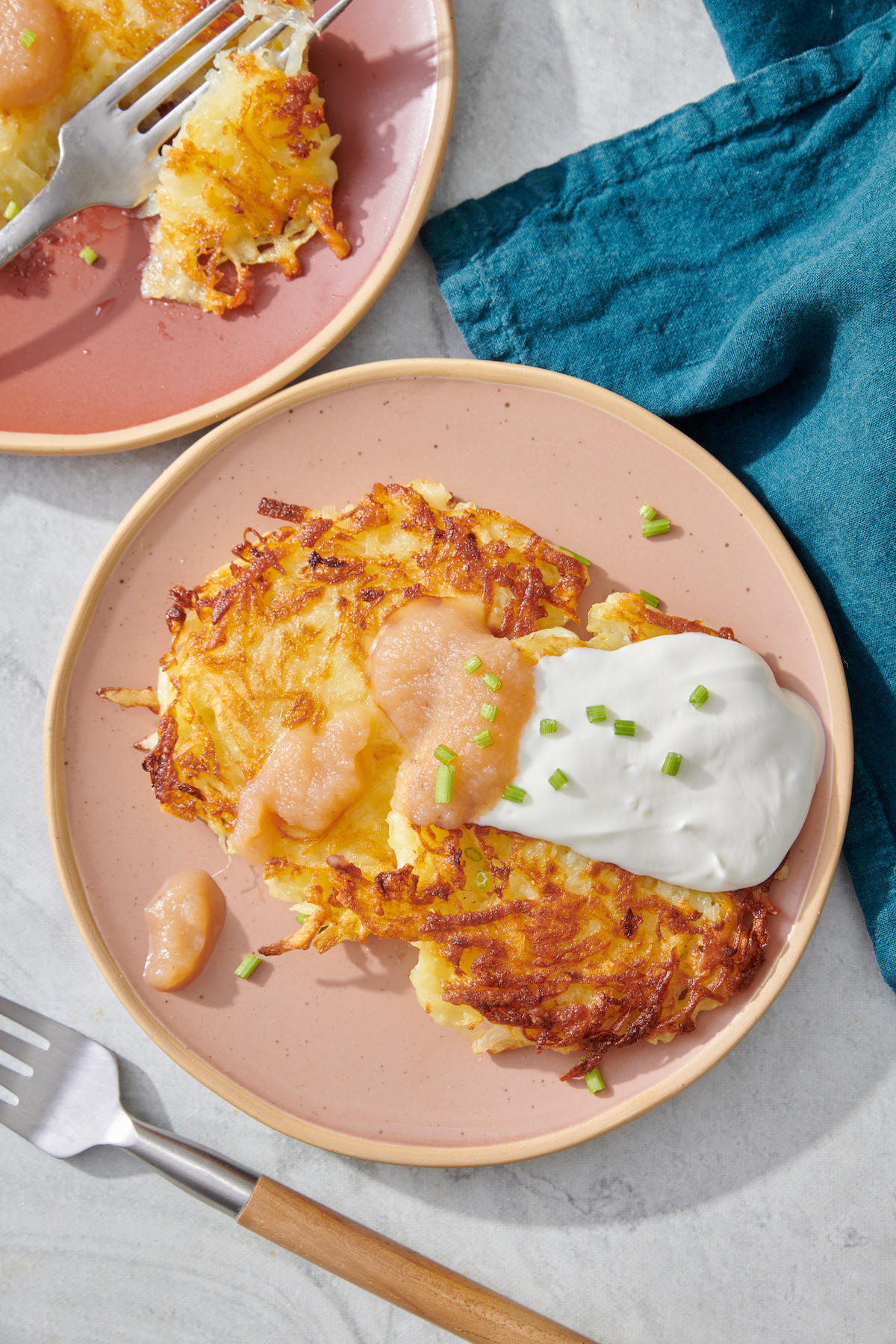 Two latkes on a plate topped with sour cream and applesauce.