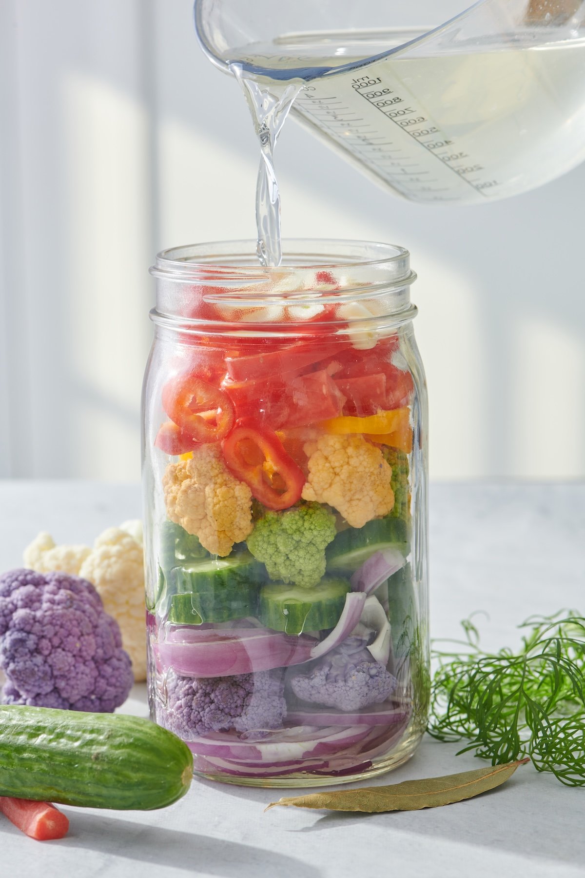 Pouring the brining liquid over the vegetables in mason jar.