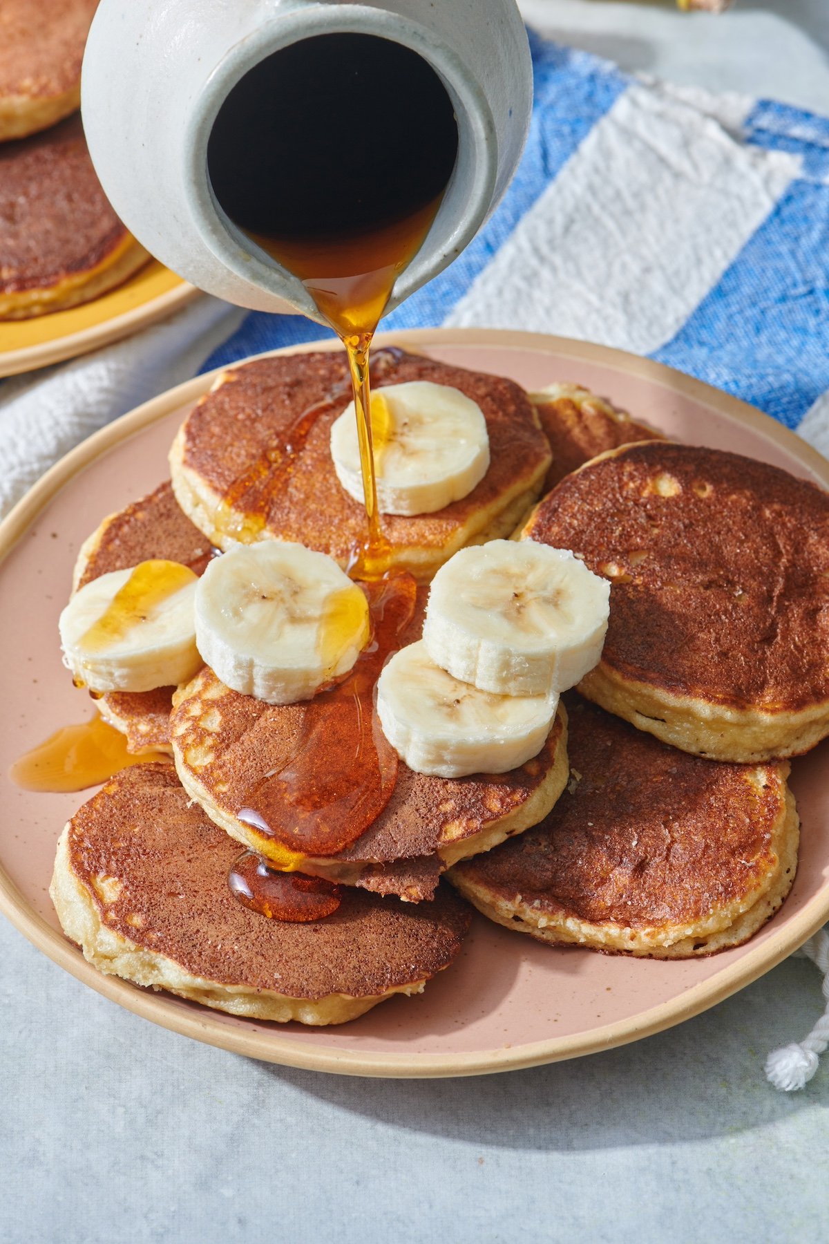 Almond flour banana pancakes on plate with maple syrup being poured on top.