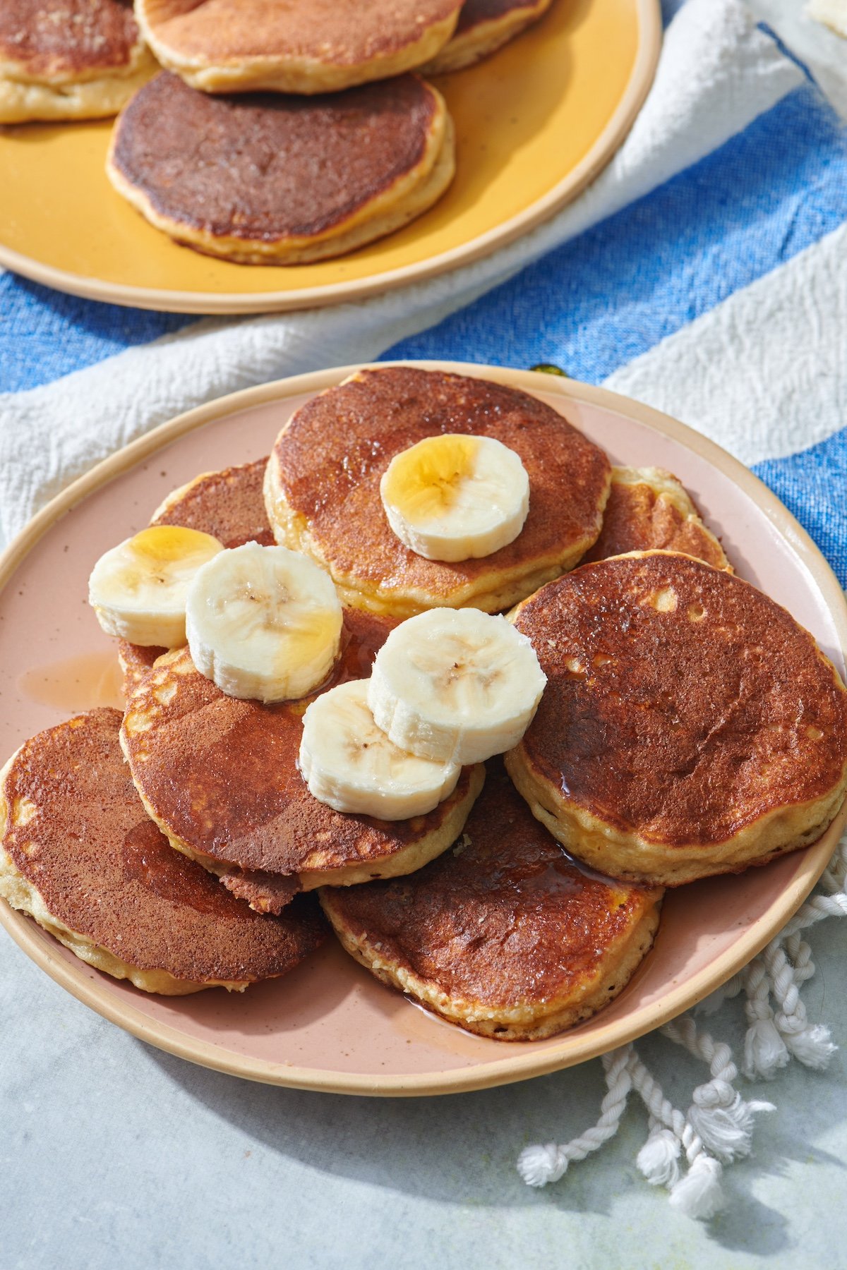 Almond flour banana pancakes on serving platter topped with sliced bananas and maple syrup.