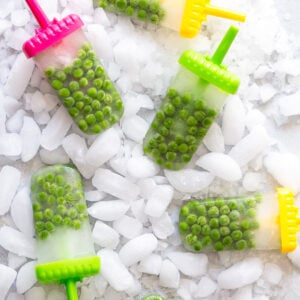 Green pea popsicles on colorful sticks arranged on crushed ice.