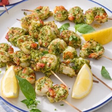 Pesto shrimp skewers on large white plate.