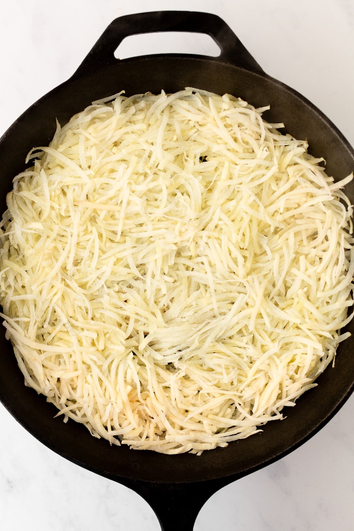 Shredded potatoes in a cast iron skillet.
