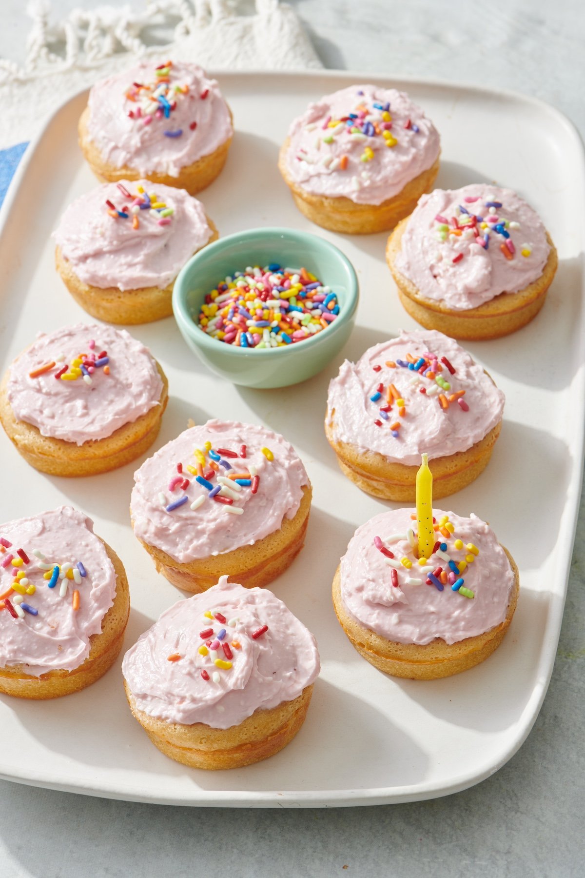 A serving platter with 10 breakfast cupcakes with jelly frosting and rainbow colored sprinkles. 