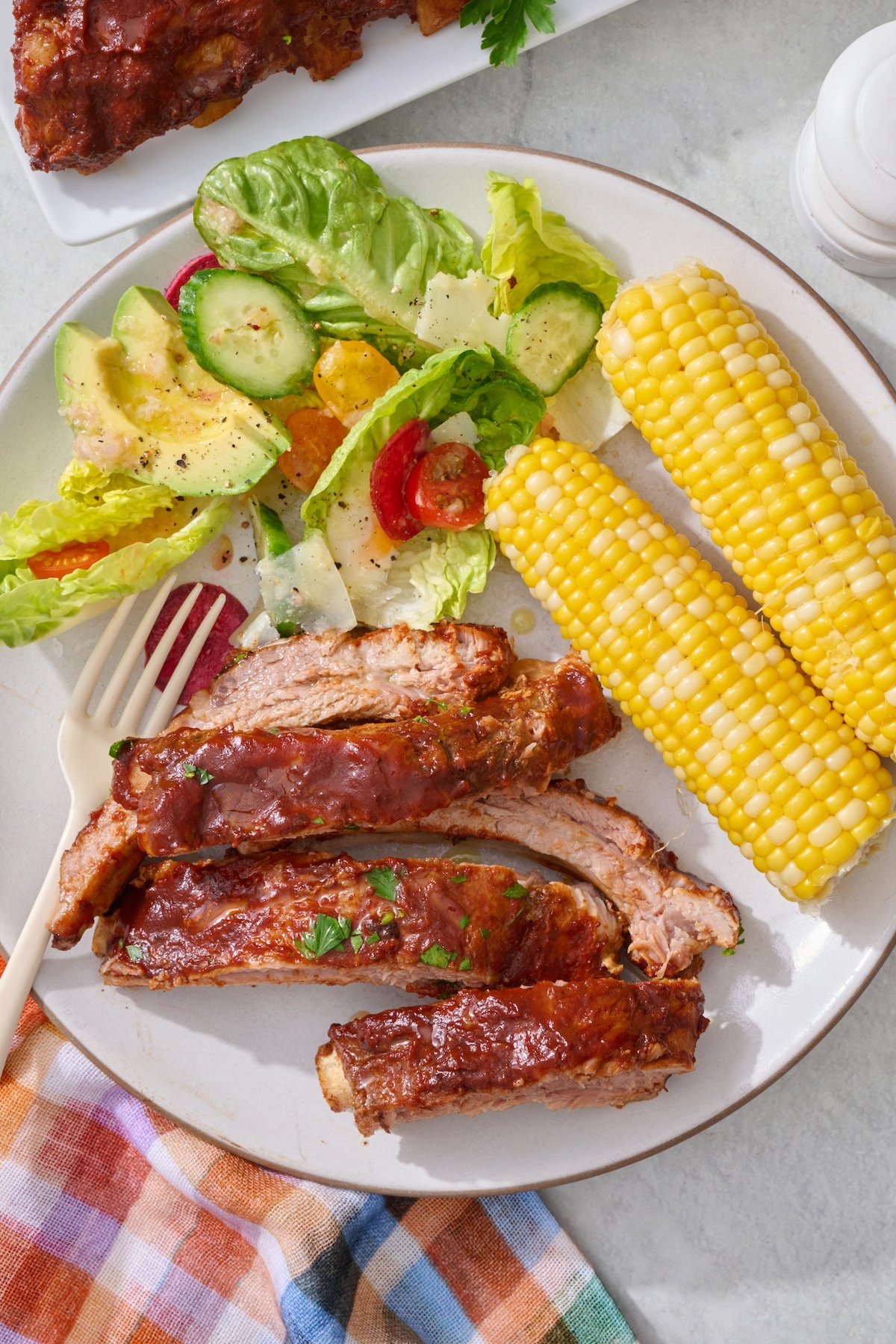 Crock pot ribs on a plate with side salad and corn on the cob.