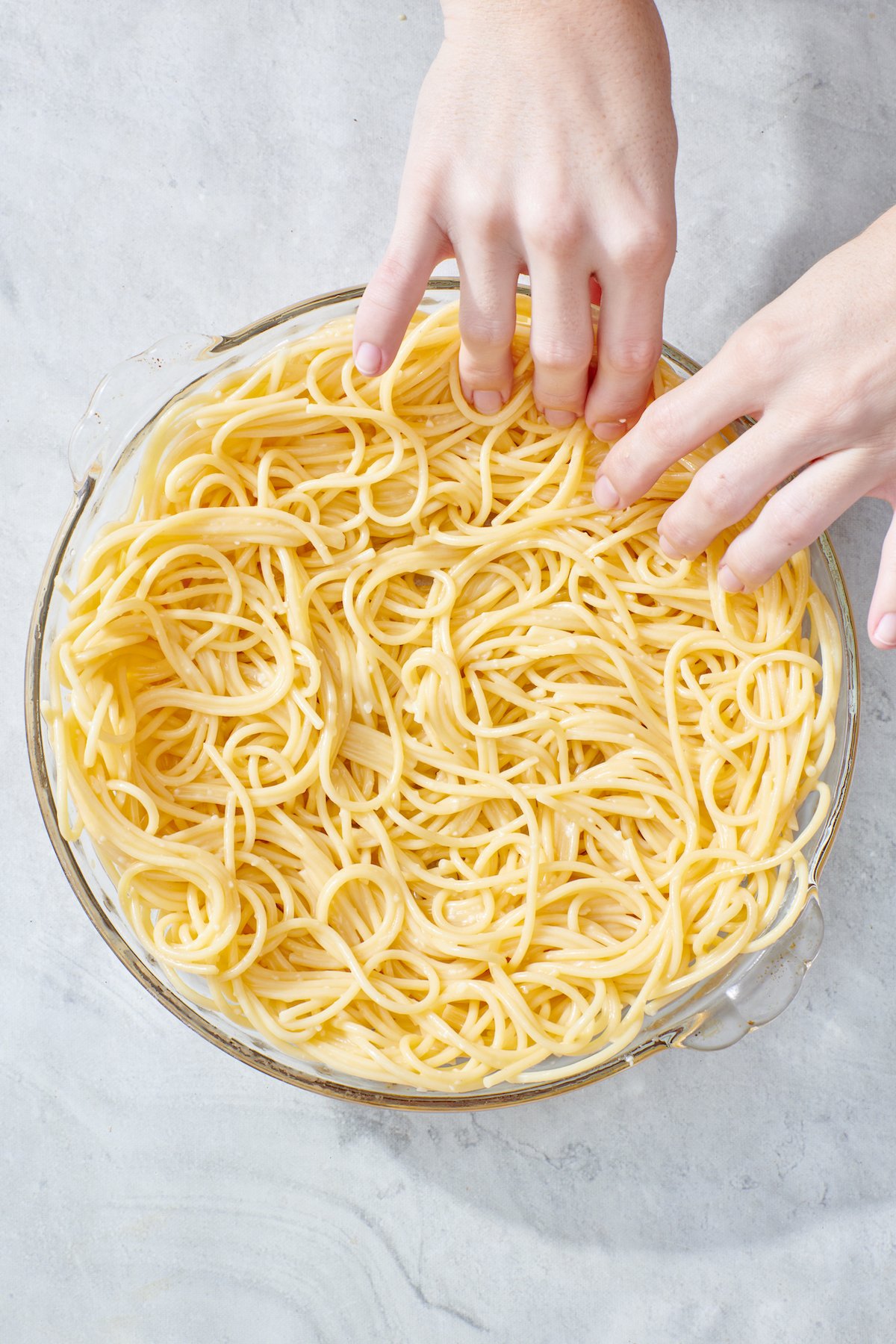 Hands spreading spaghetti mixture into deep dish pie plate.