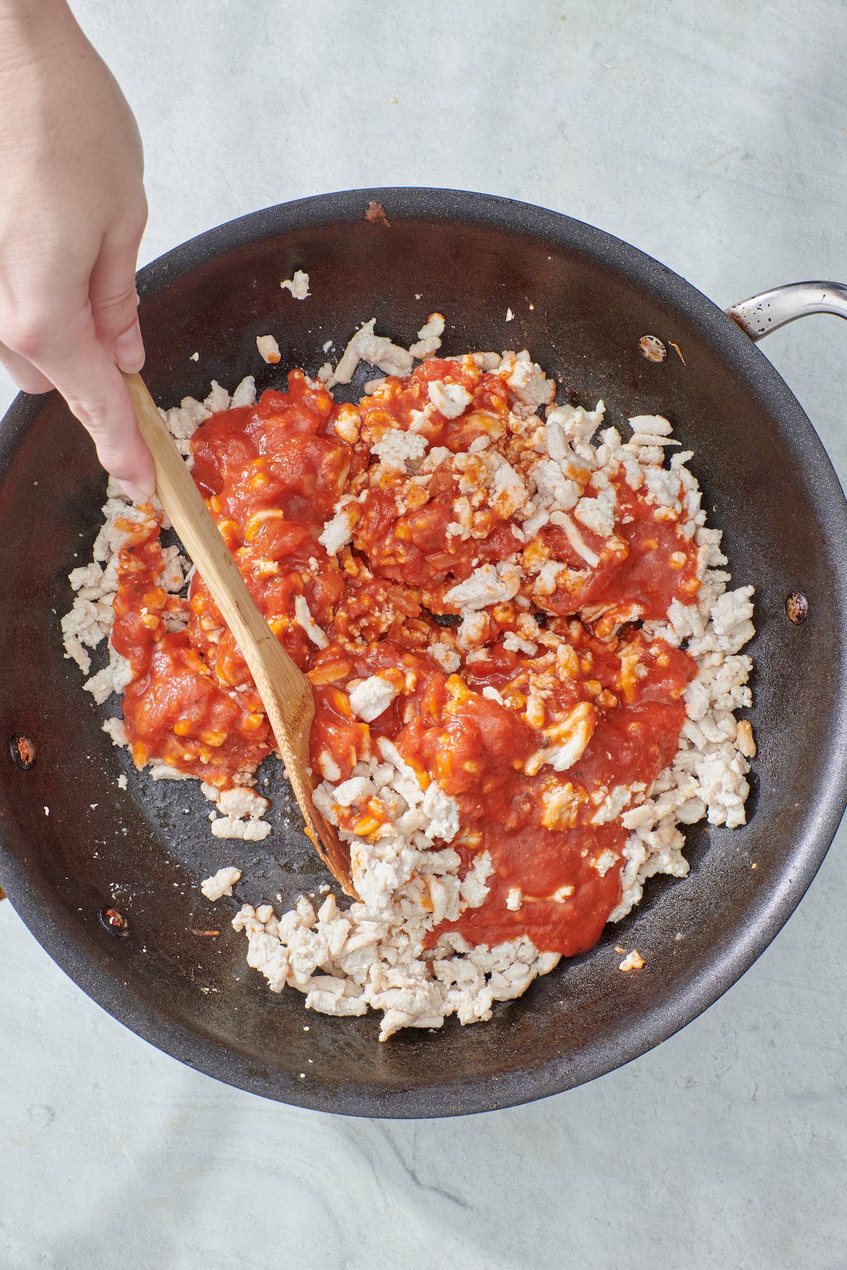 Hand mixing tomato sauce with cooked ground turkey.