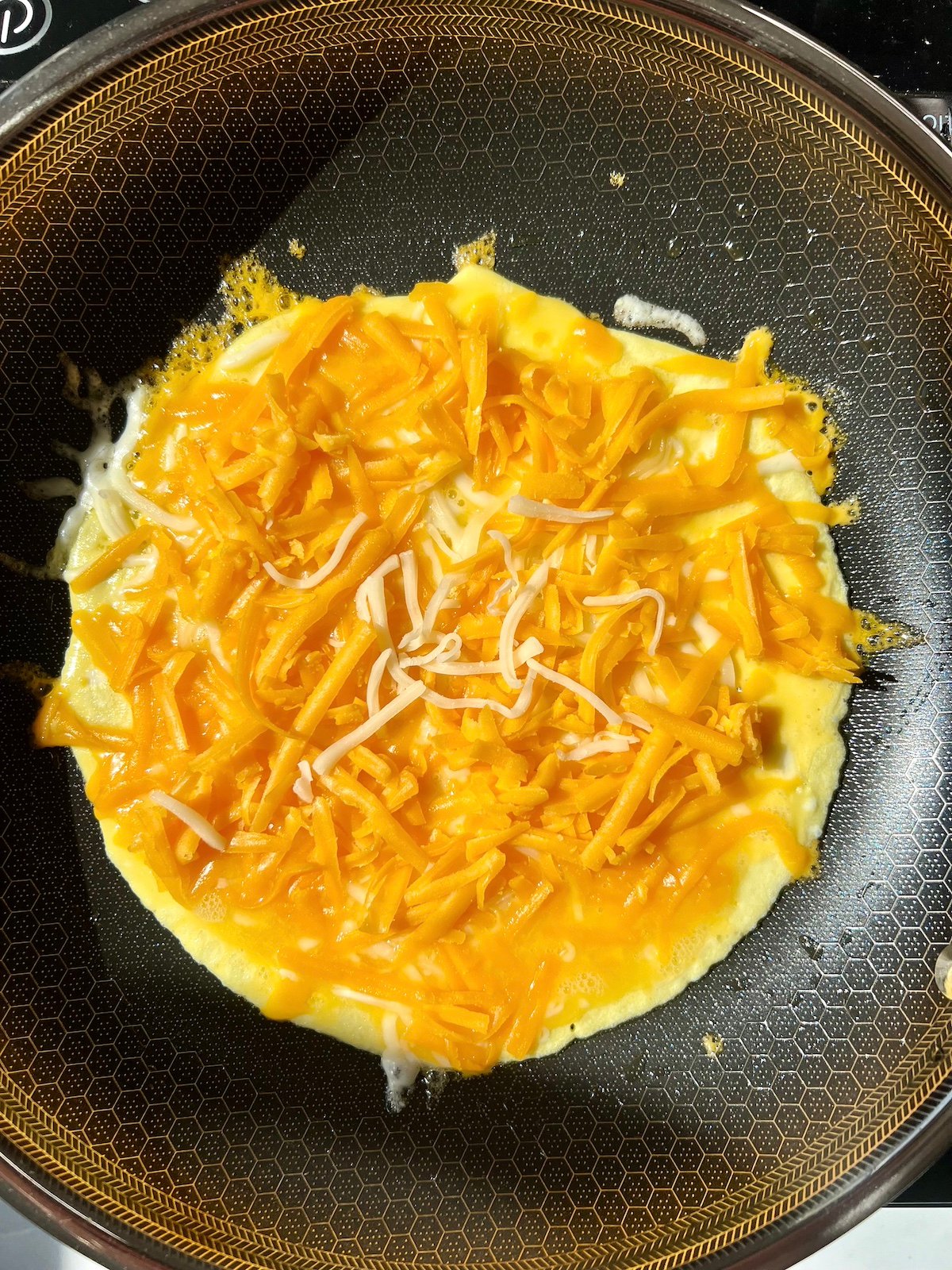Shredded cheese on top of omelette in pan.