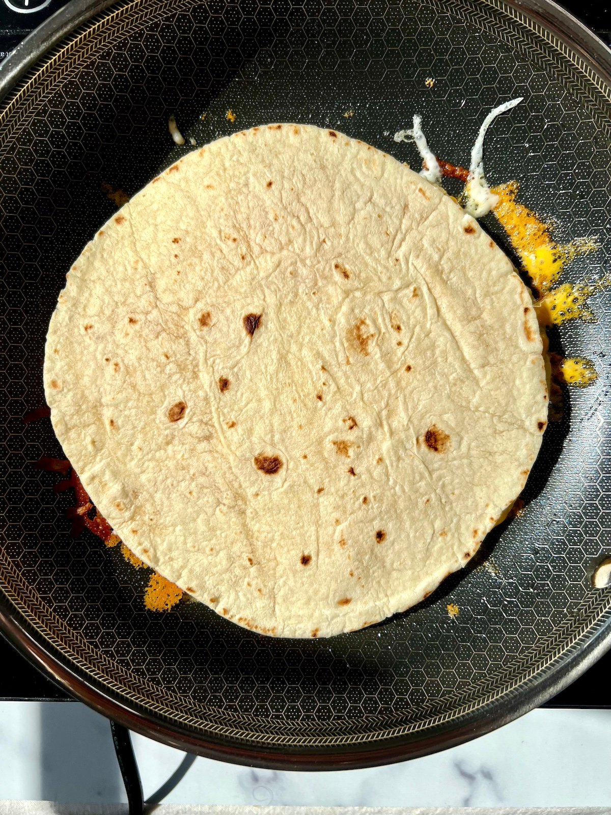 Tortilla on top of  egg in pan.