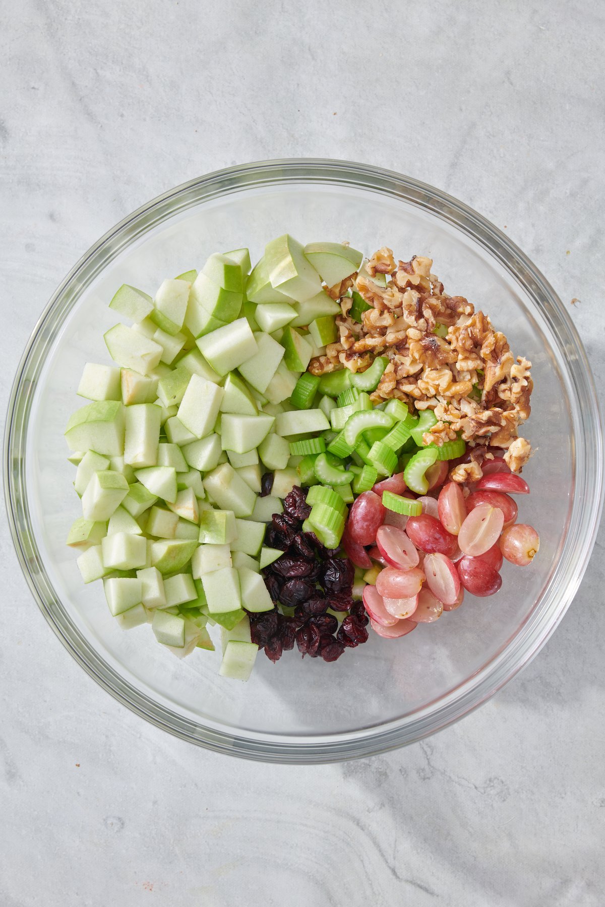 Celery, apples, walnuts, grapes and cranberries in mixing bowl.