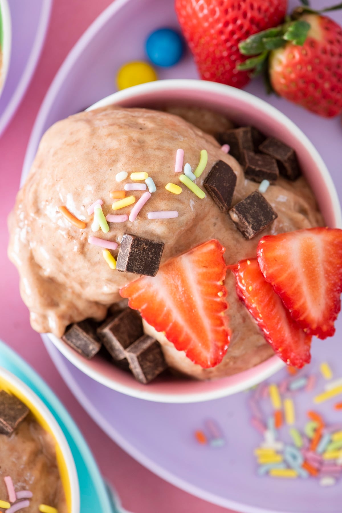 A scoop of chocolate banana ice cream topped with strawberries and chocolate chips.