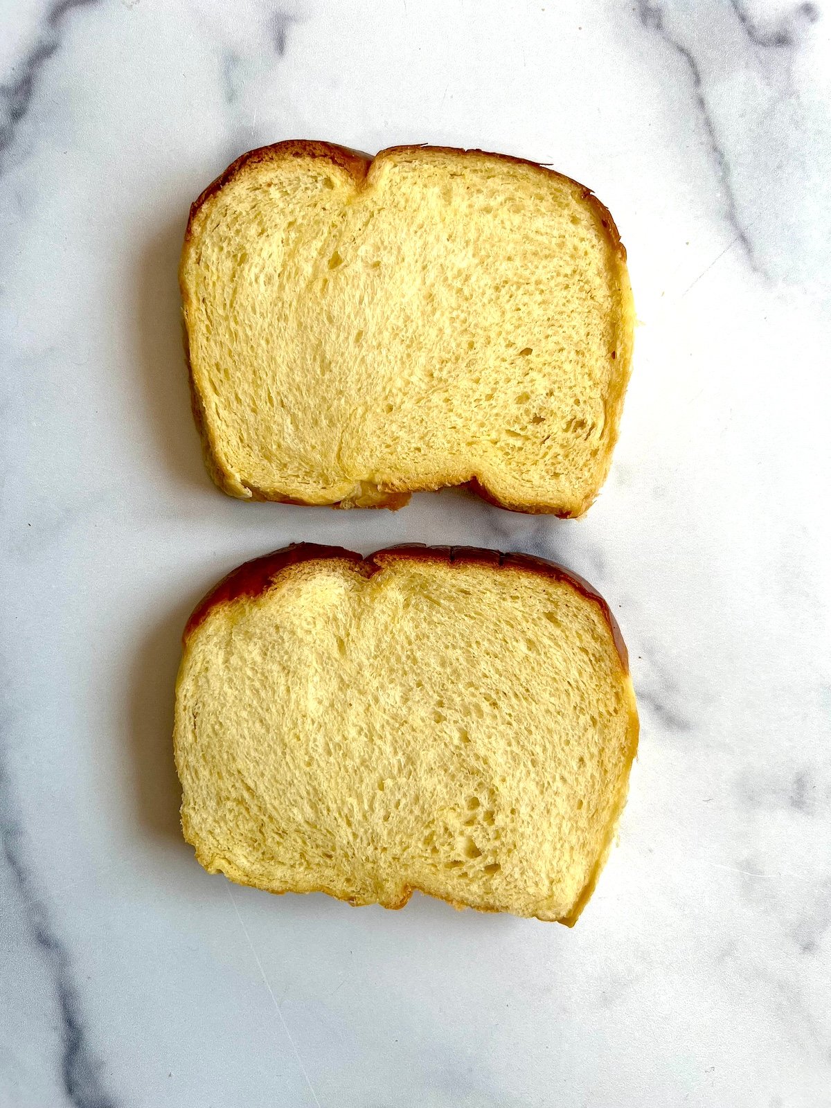 Two slices sandwich bread on marble countertop.