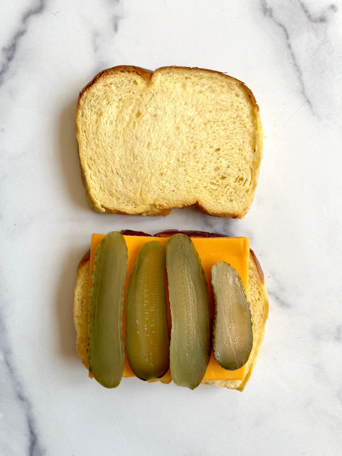 Open faced sandwich with cheddar cheese slice and sliced pickles.