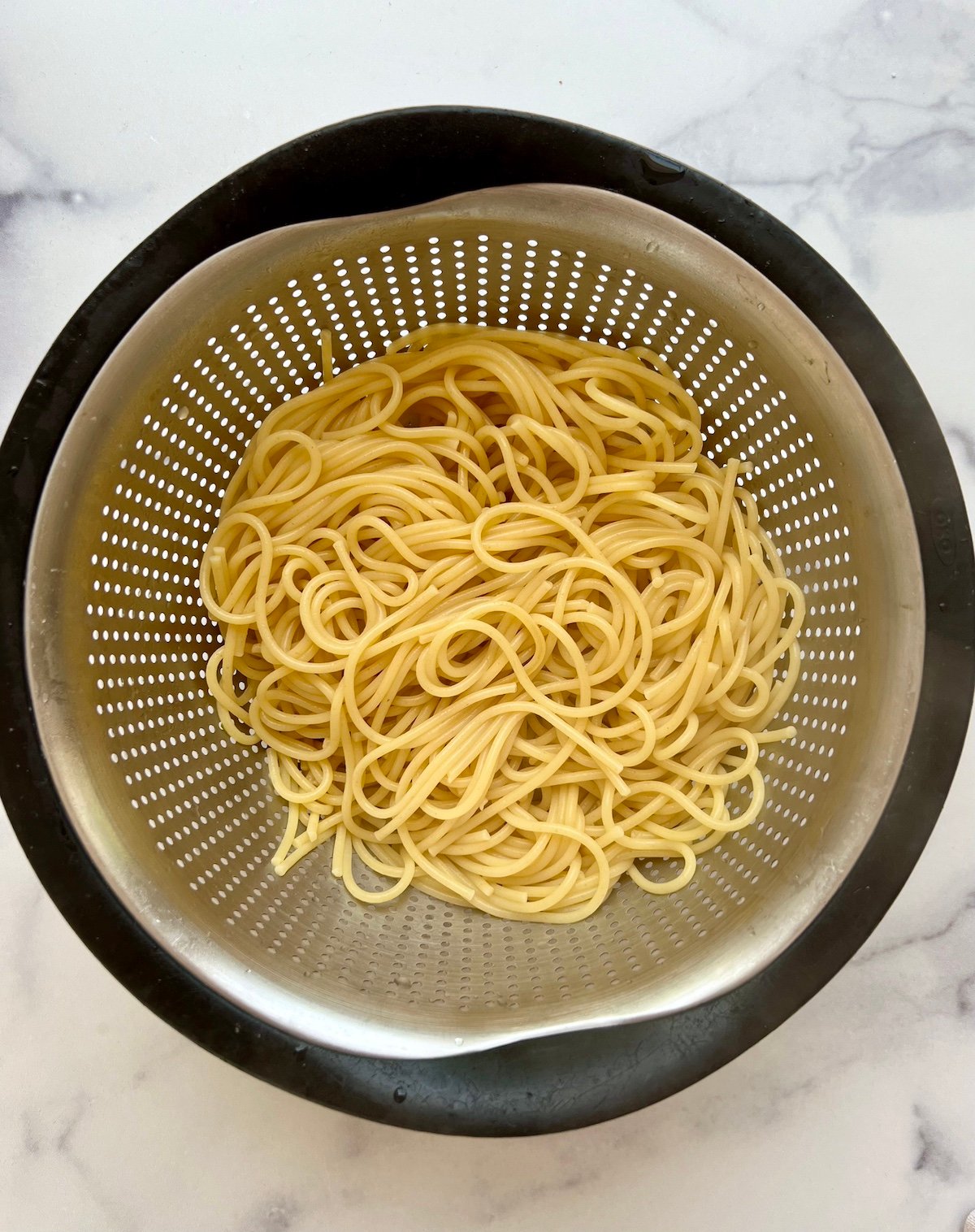 Cooked spaghetti noodles in strainer.