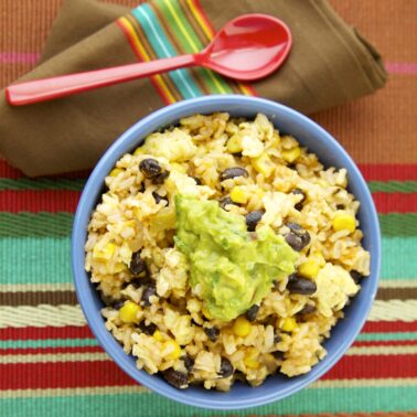 Mexican fried rice with black beans, corn, and guacamole served in a blue bowl.