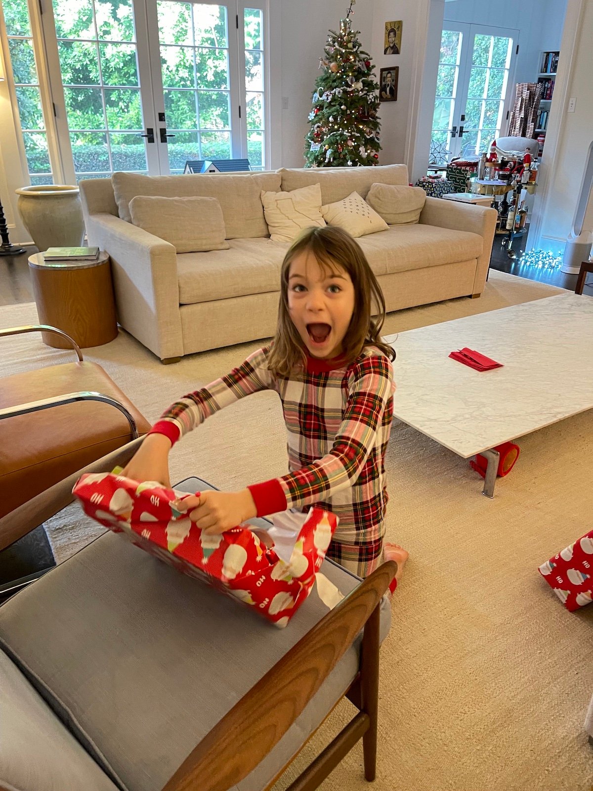 Young girl with excited expression opening a holiday gift.