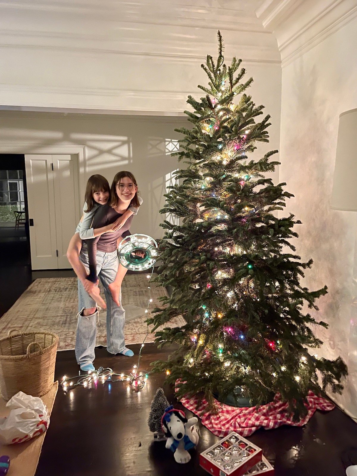 Two siblings posed next to a Christmas tree they're decorating.