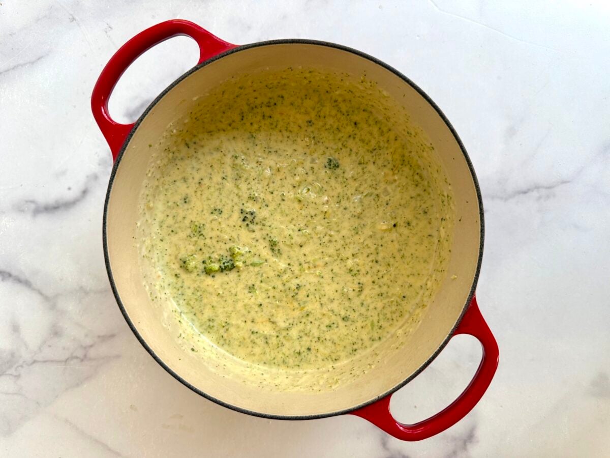 Creamy broccoli cheddar soup in a red enameled cast iron pot.