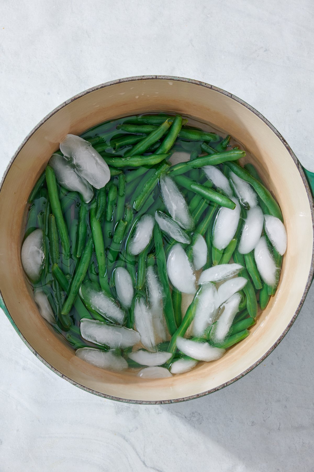 Cooked green beans in pot with water and ice.