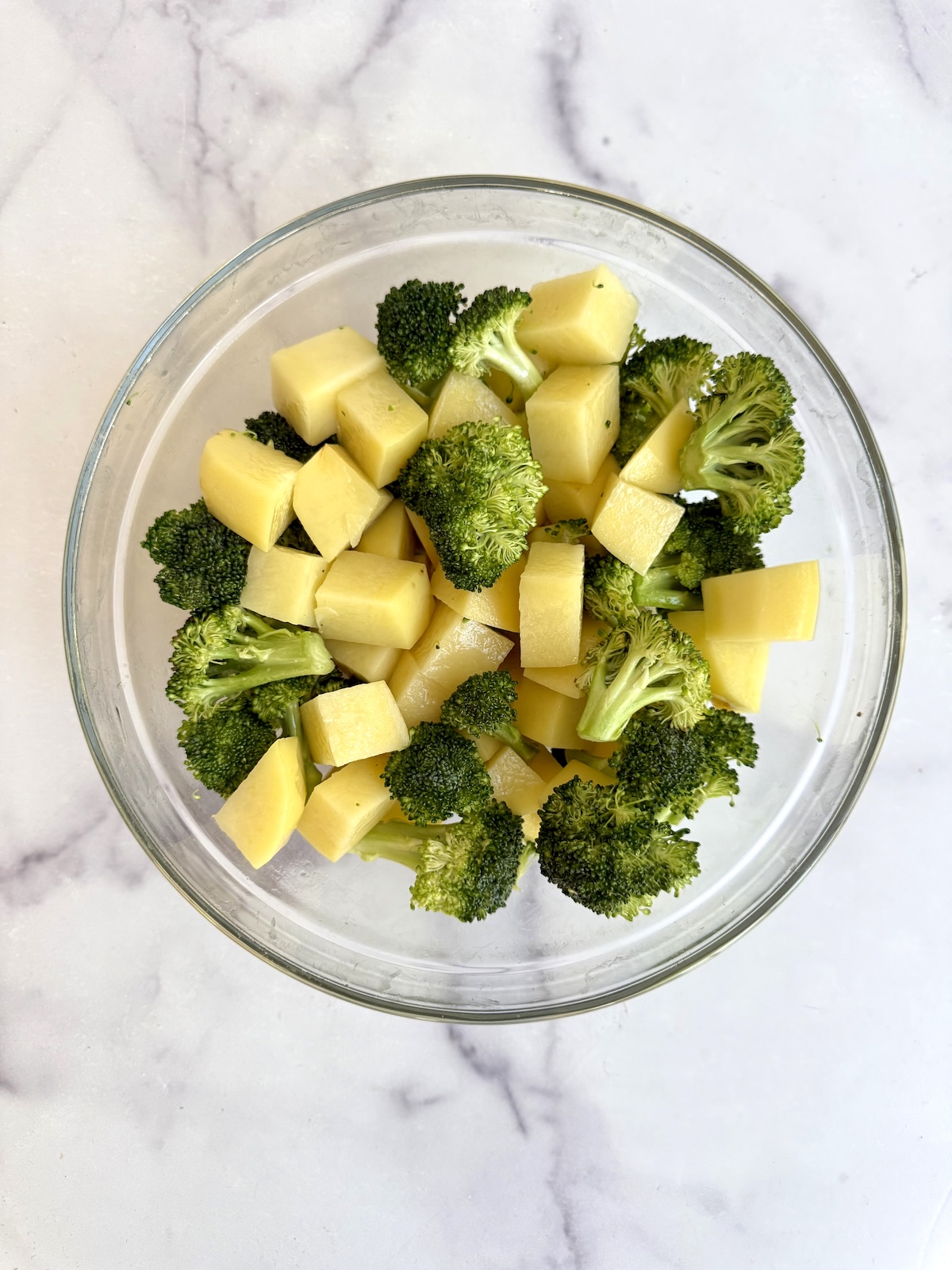 Cubed potatoes and broccoli florets tossed together in a glass bowl.