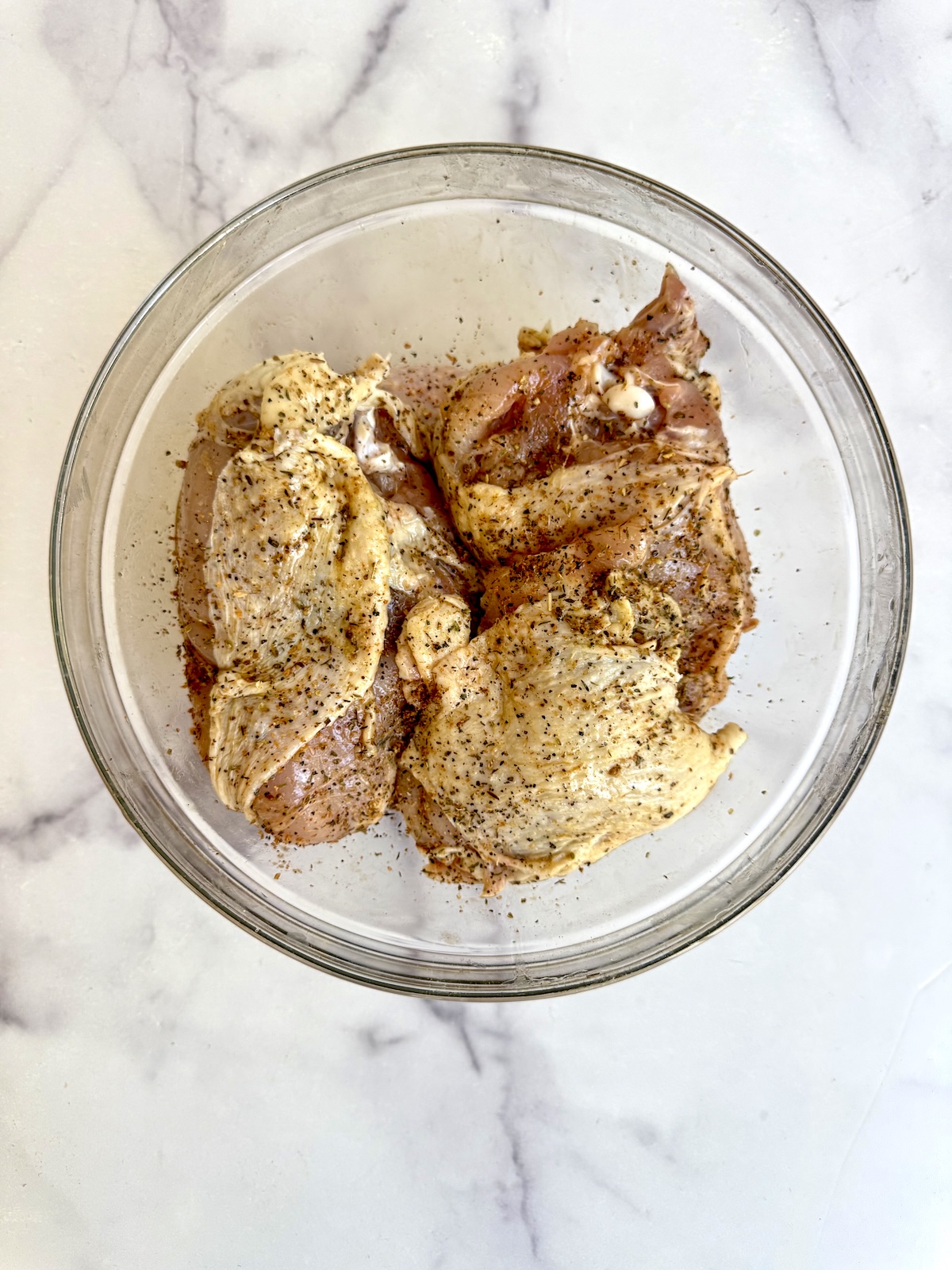 Bone-in chicken pieces coated in za'atar and olive oil in a glass bowl.