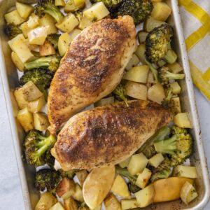 Two za'atar sheet pan chicken breasts roasted with broccoli, potatoes, and lemon on a baking sheet.