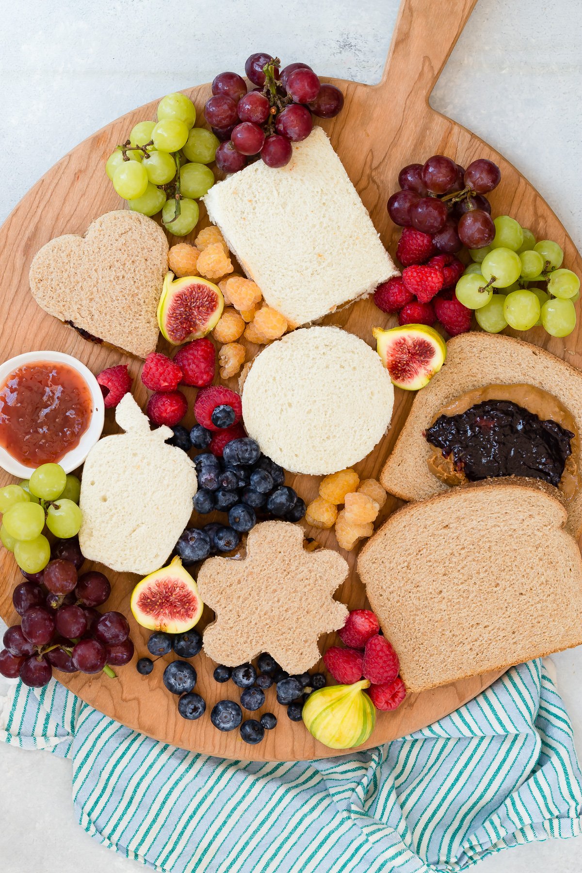 Homemade uncrustables on wooden cutting board surrounded by fruits.