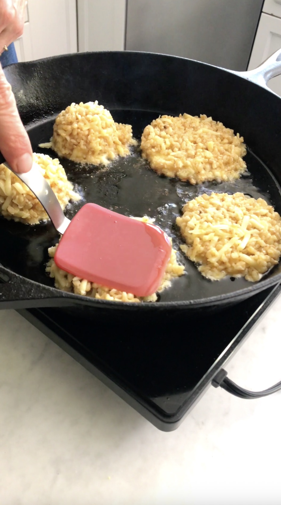 Brown rice cake patties pressed flat in a cast iron skillet with a spatula.