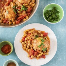 Easy Moroccan chicken with chickpeas and tomatoes served on a white plate alongside the pan.