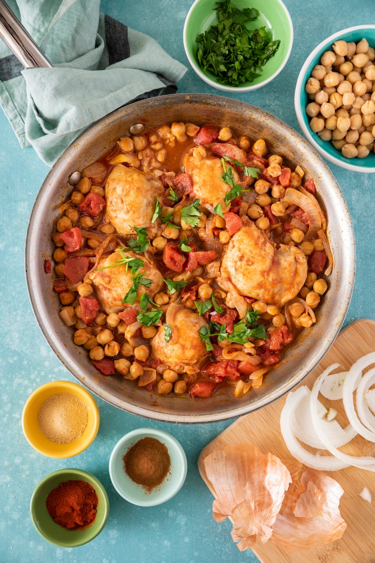 Easy Moroccan chicken with chickpeas simmering in a spiced tomato sauce with ingredients surrounding the pan.