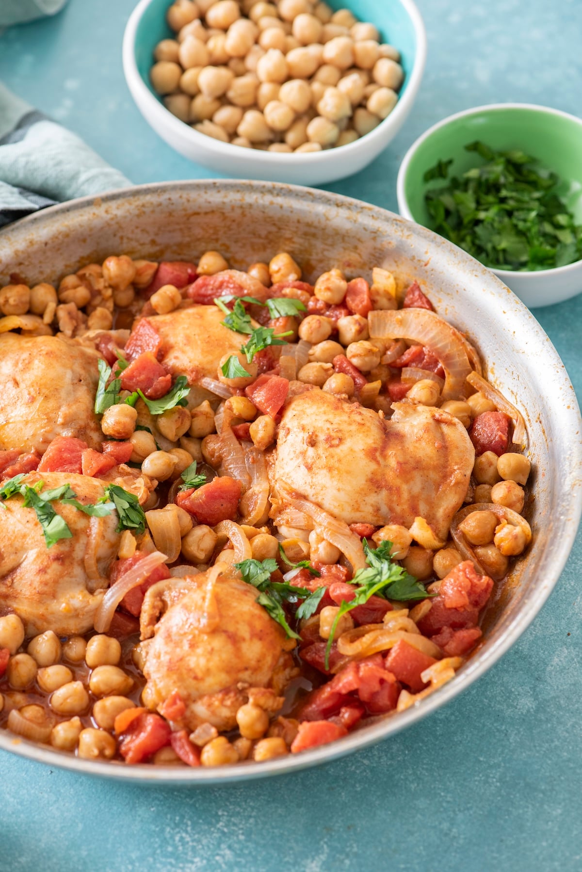 Braised Moroccan chicken thighs with chickpeas, tomatoes, and fresh parsley in a skillet.