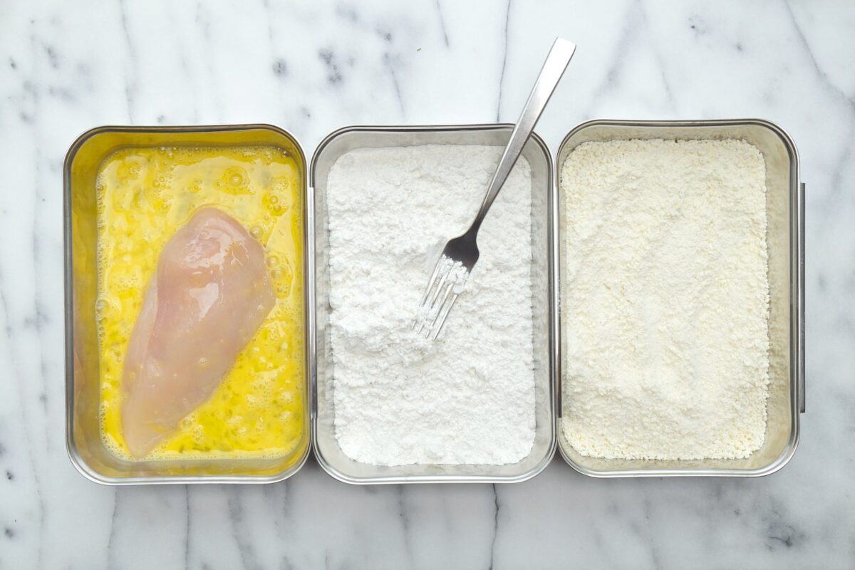 A chicken breast dredged through flour, egg, and panko in a three-step breading station.