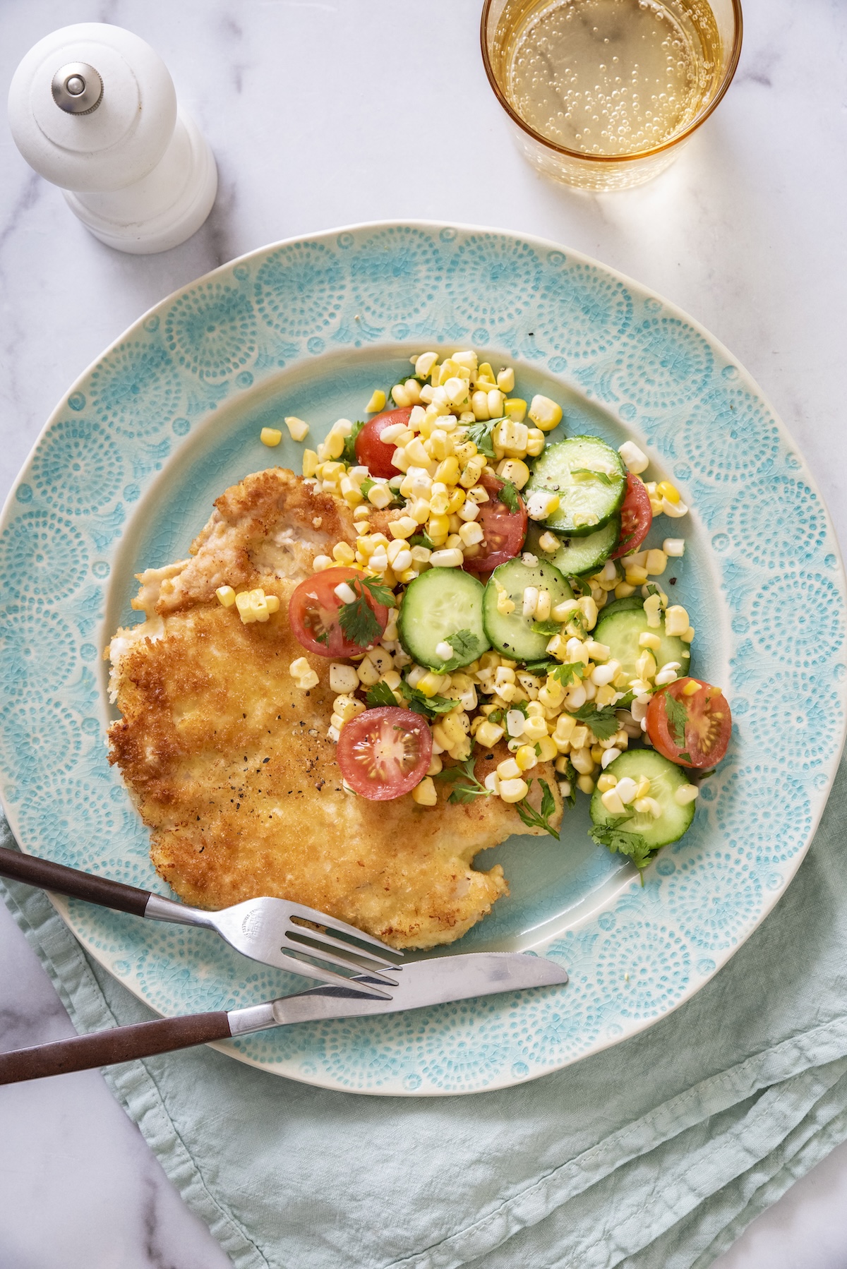A single serving of crispy chicken paillard with summer corn salad on a blue plate.