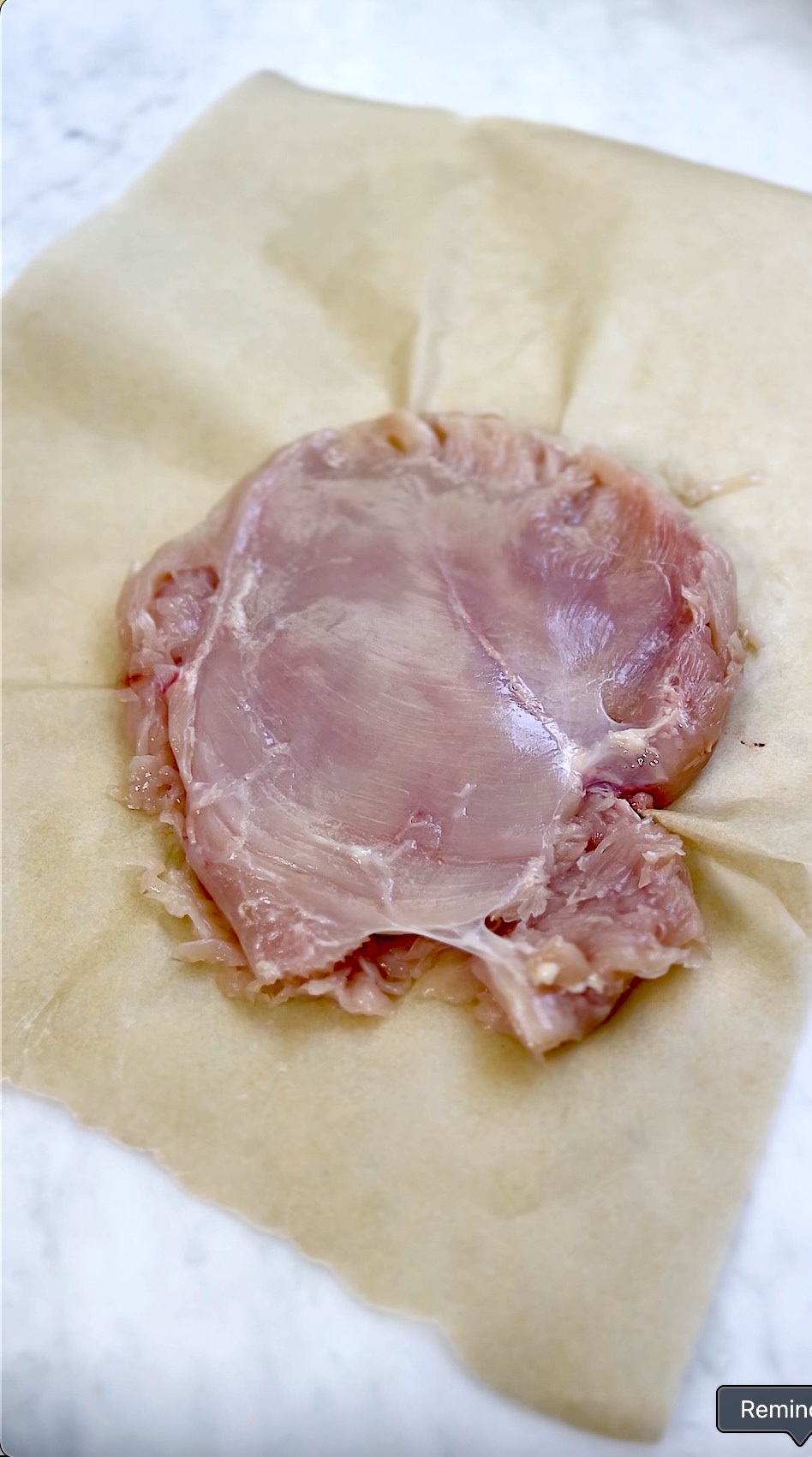 A boneless chicken breast pounded thin on a sheet of parchment paper.