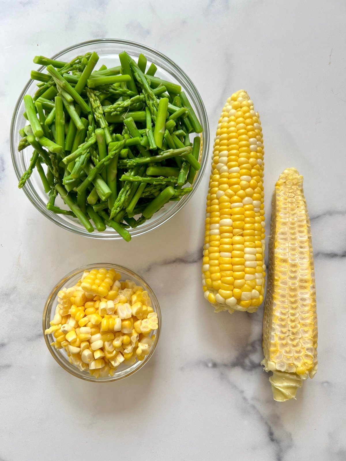 Chopped asparagus in a bowl and corn off the cob in a bowl.
