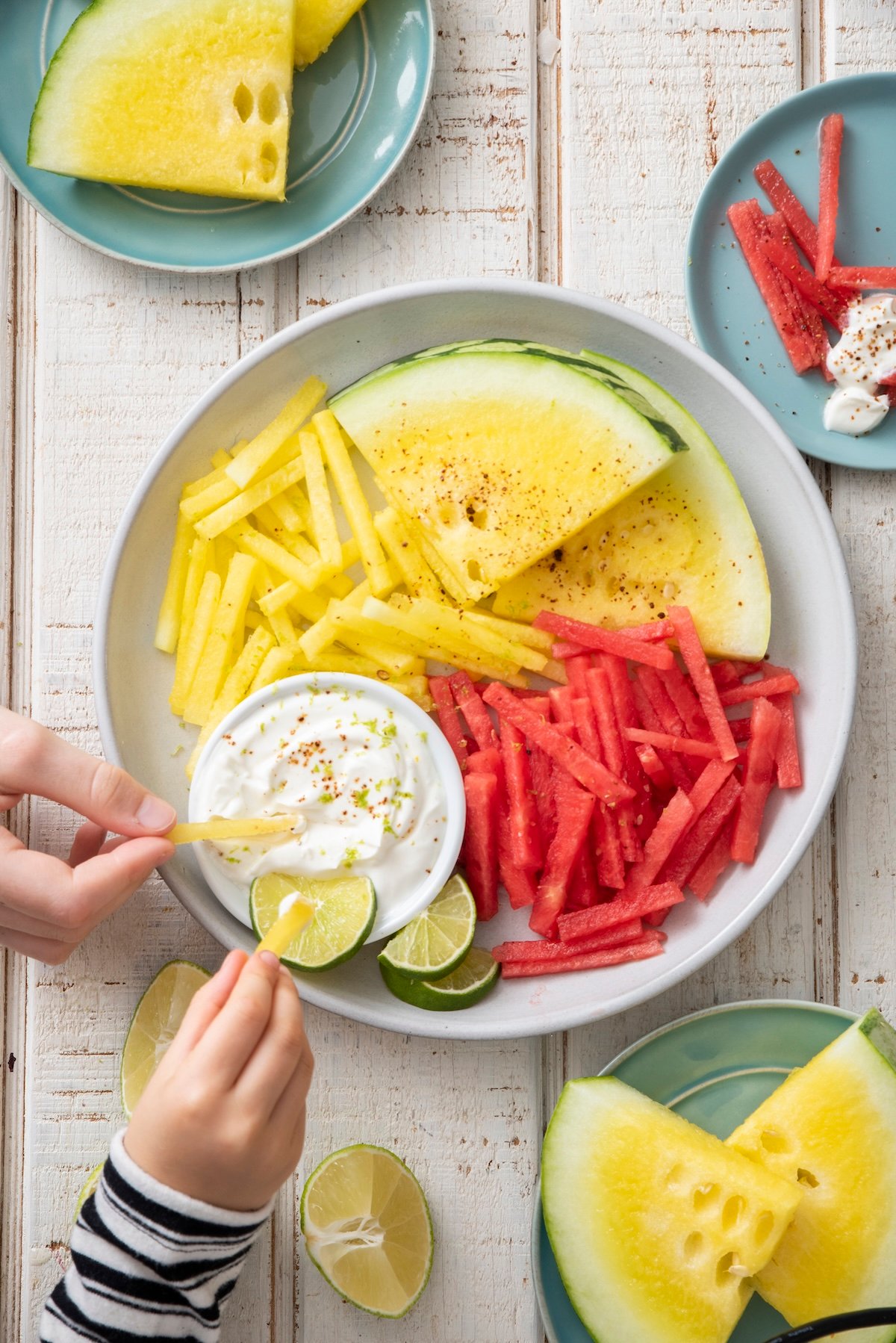 Hands dipping watermelon fries in yogurt dip.