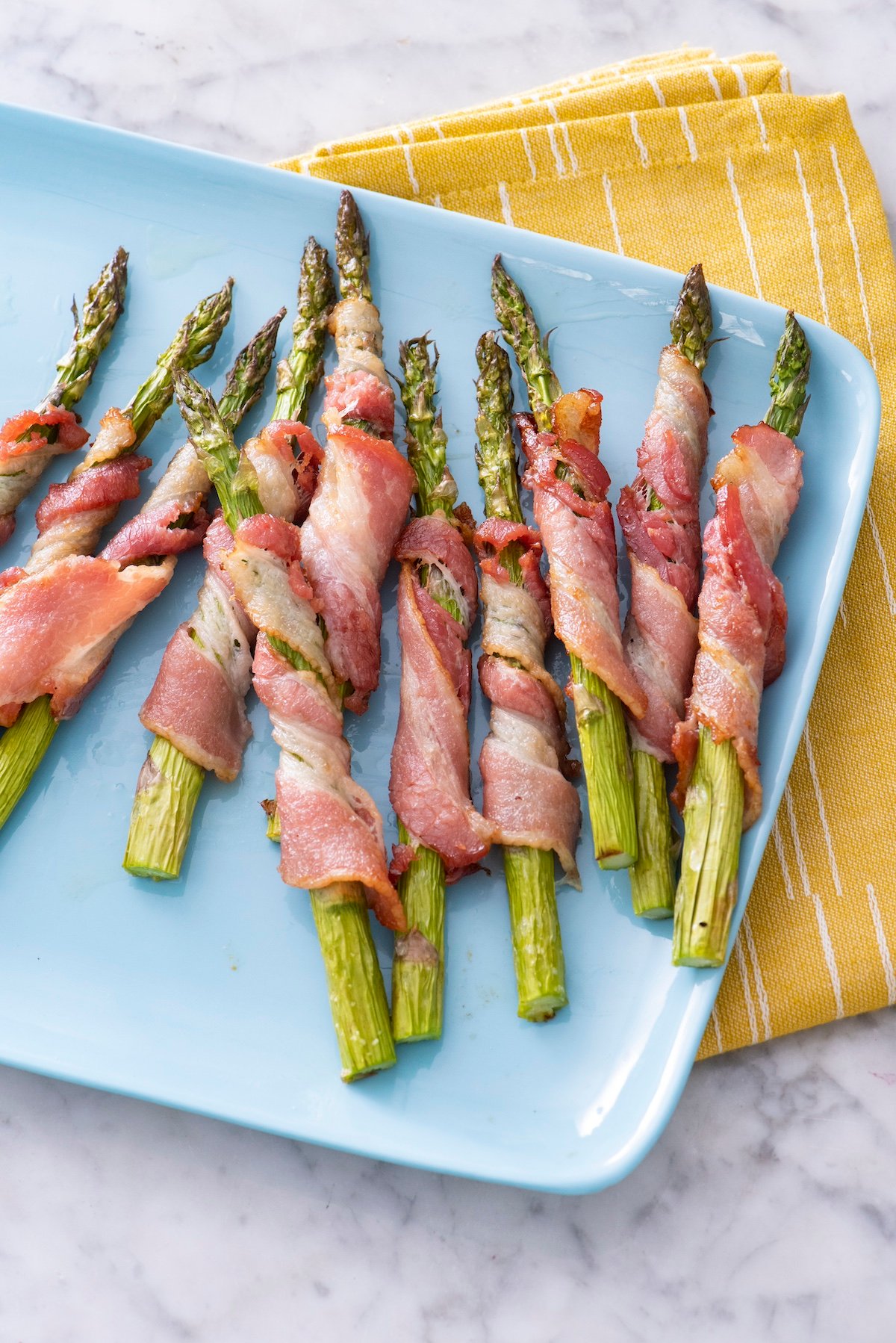 air fryer bacon wrapped asparagus on a blue serving platter.