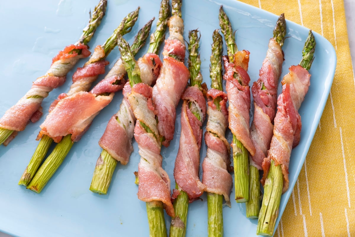 air fried bacon wrapped asparagus on blue serving platter.