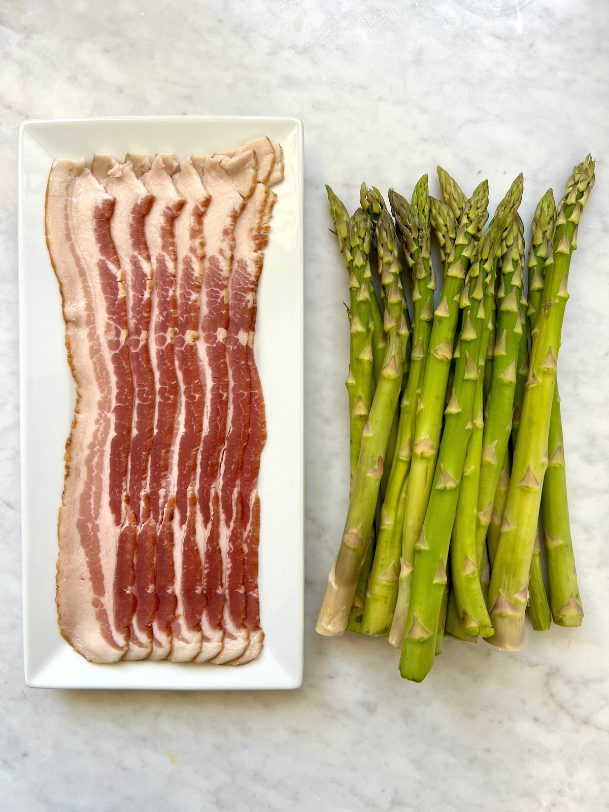 bacon on a plate next to a bundle of asparagus.