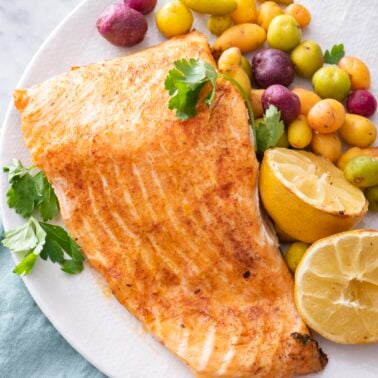 Air fryer salmon on a plate with potatoes and lemon halves.