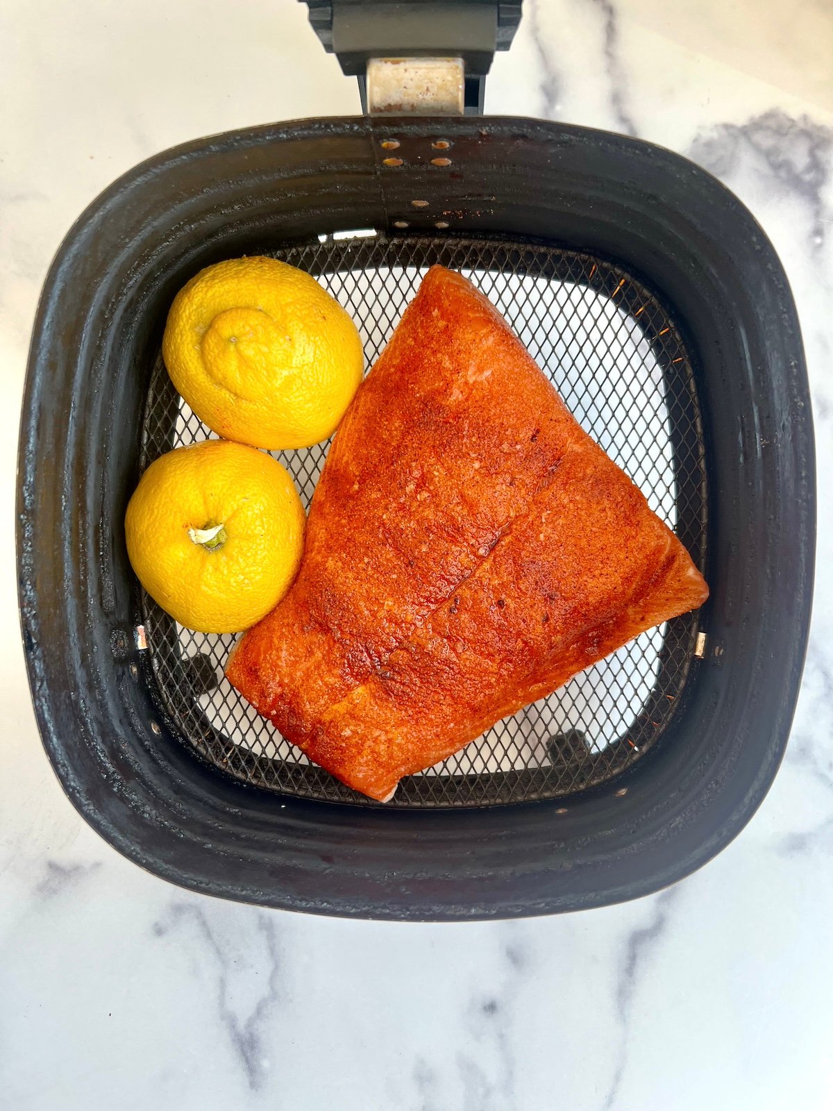 Salmon in air fryer basket with lemon halves.