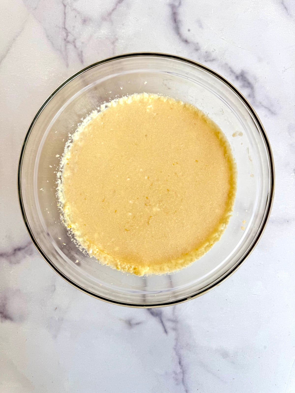 Wet batter with milk and eggs added to the creamed butter mixture in a glass bowl.