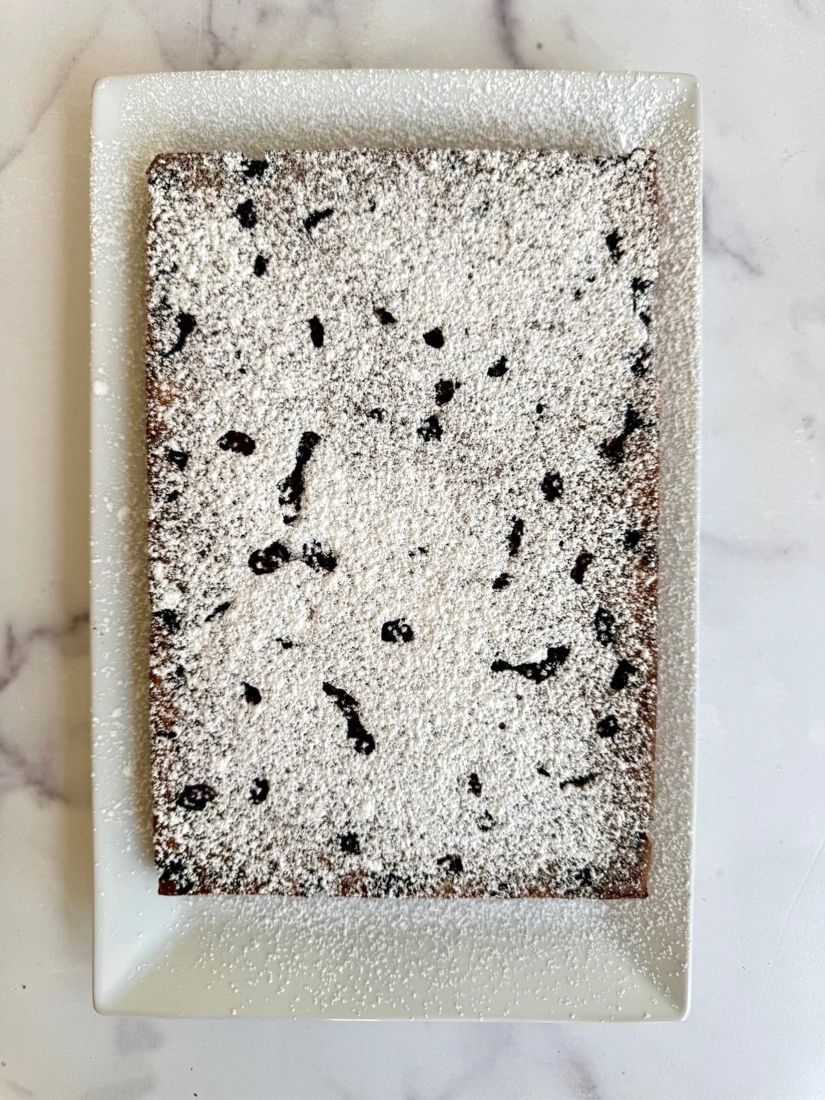 Blackberry tea cake dusted with powdered sugar on a white serving platter.