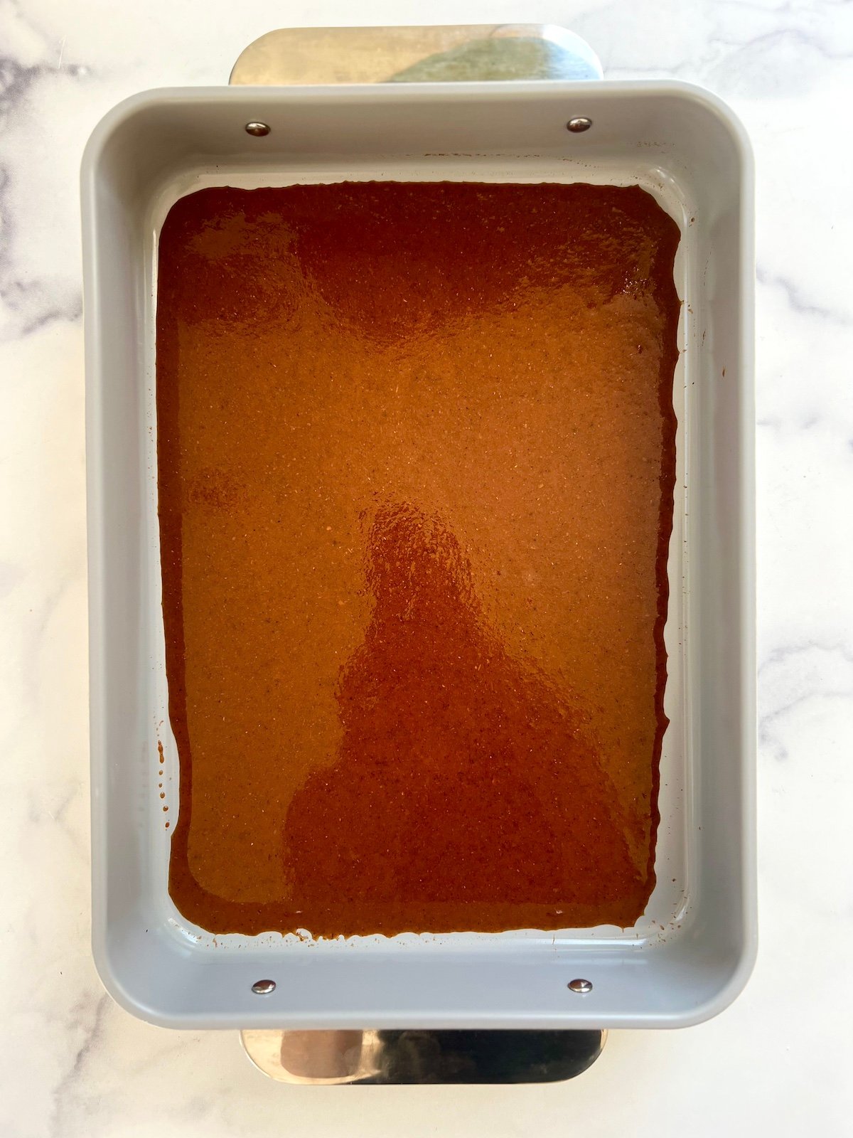 Enchiladas sauce covering the bottom of a baking dish.