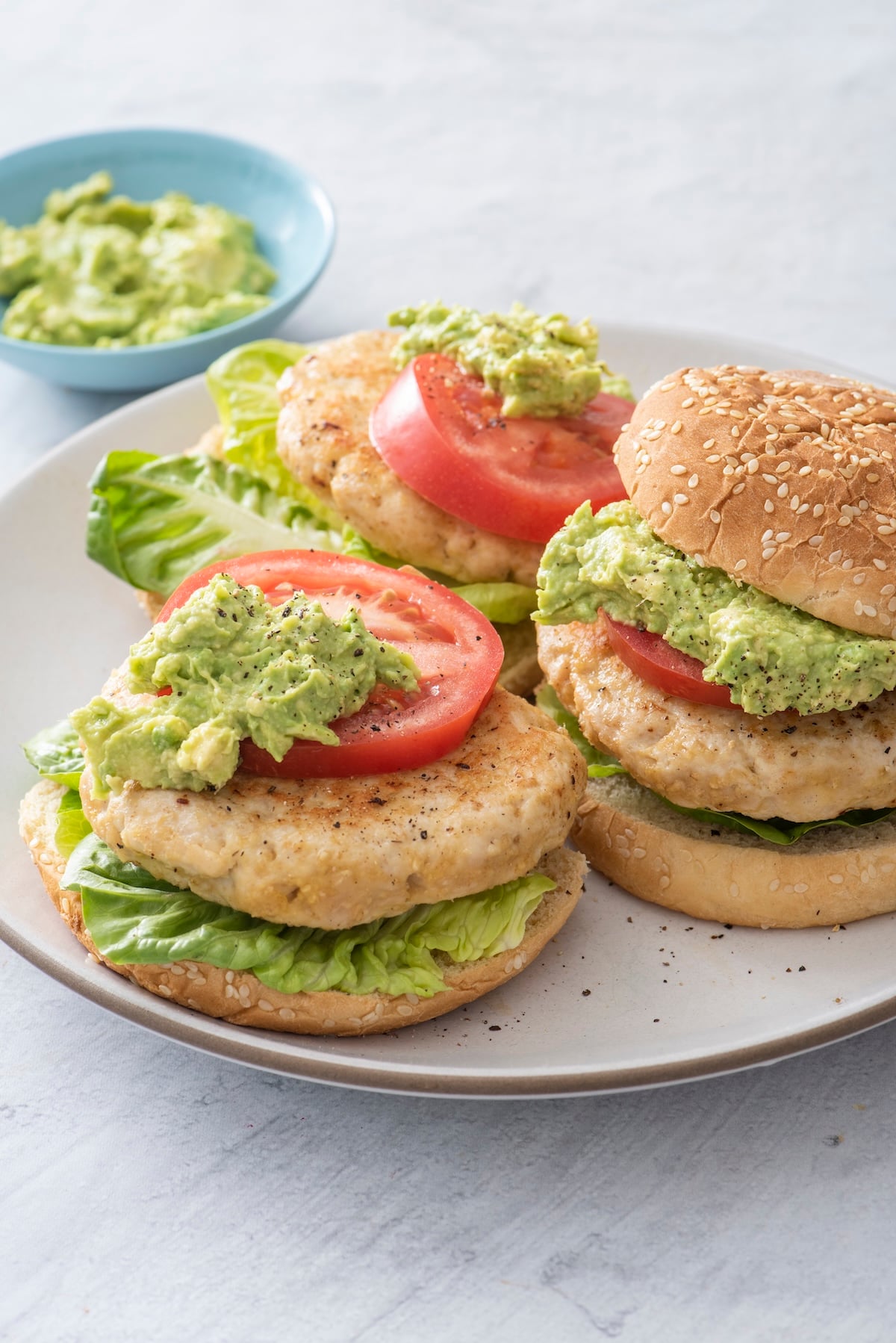 Juicy turkey burgers with oats served on sesame buns with guacamole, tomato, and lettuce on a white plate.