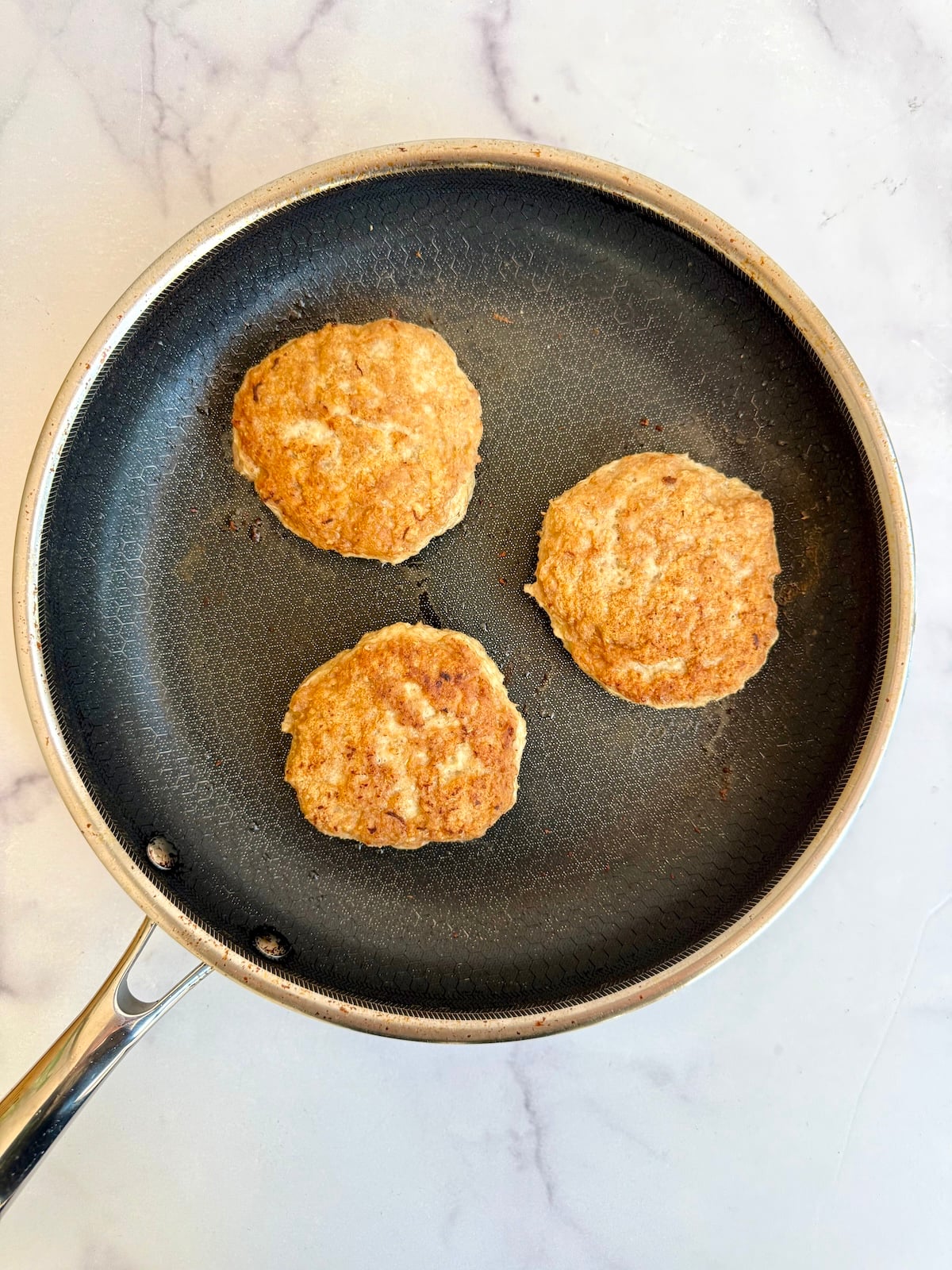 Three turkey burger patties cooking in a skillet over medium heat.